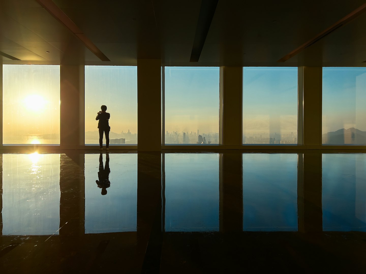 A person stands at a floor-to-ceiling window overlooking a cityscape.
