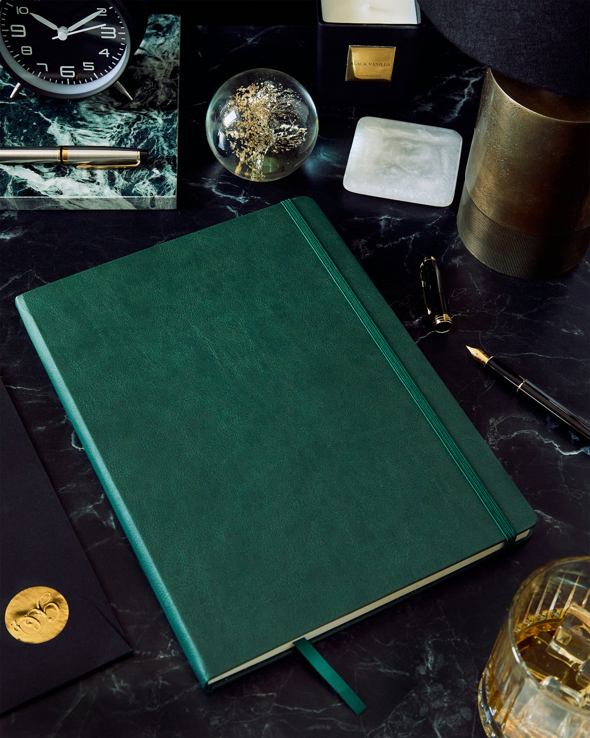 Green leather notebook and desk accessories on a marble surface.